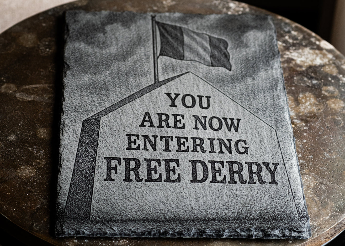 Textile with 'You are now entering Free Derry' printed on it, displayed on a round stone surface.