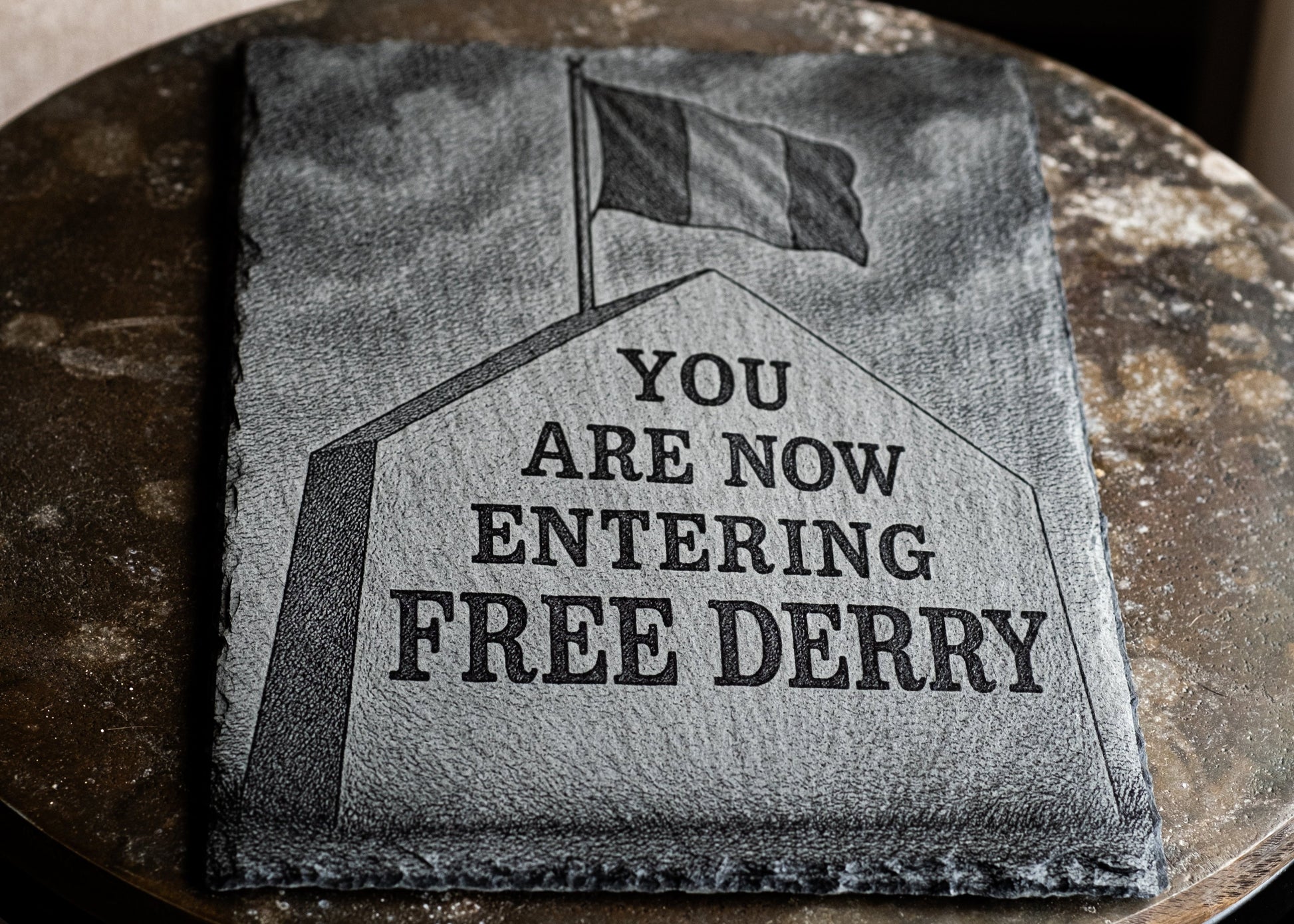 Textile with 'You are now entering Free Derry' printed on it, displayed on a round stone surface.